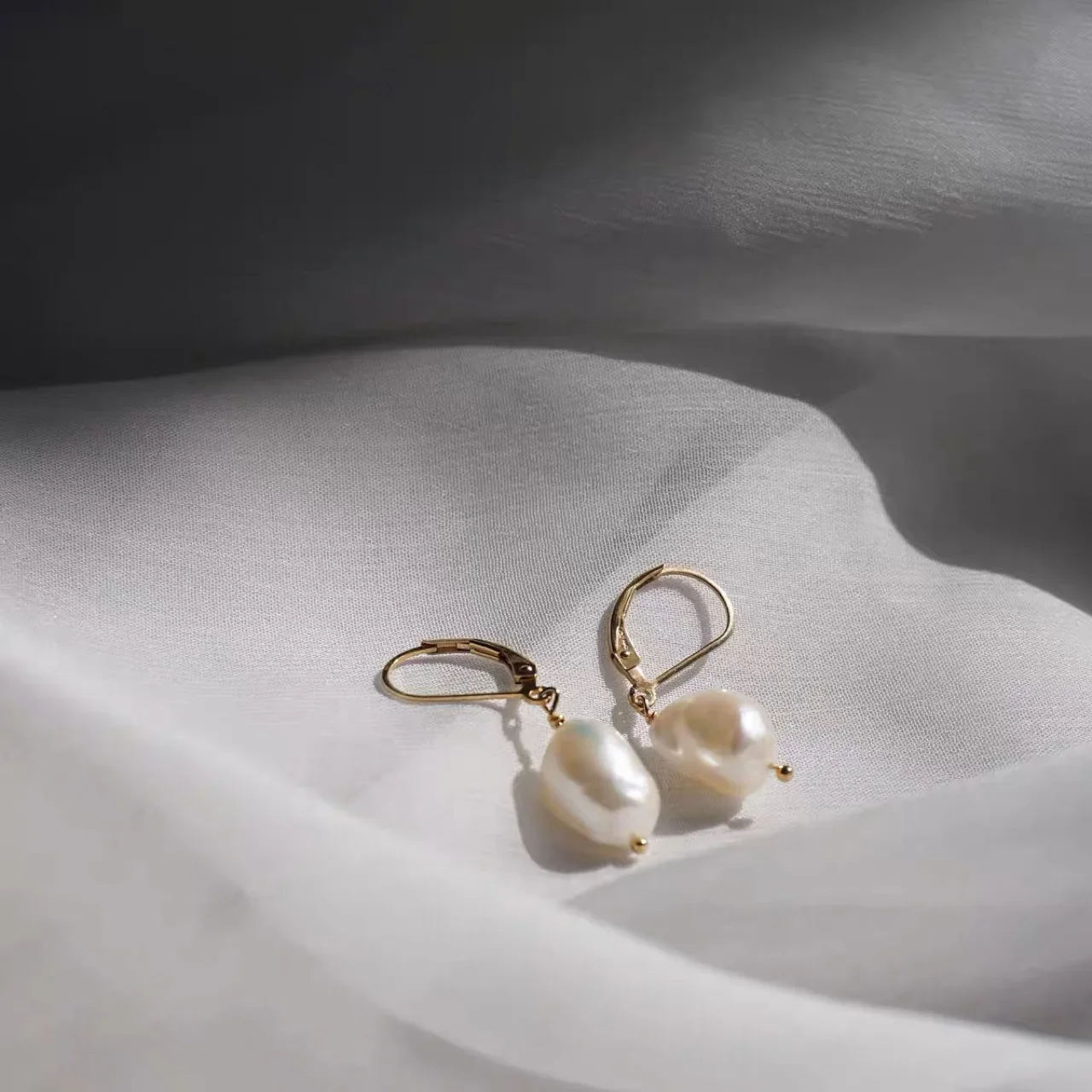 Elegant freshwater pearl drop earrings with gold lever-back hooks on white fabric background.