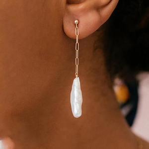 Gold earring with a pearl drop worn by a person