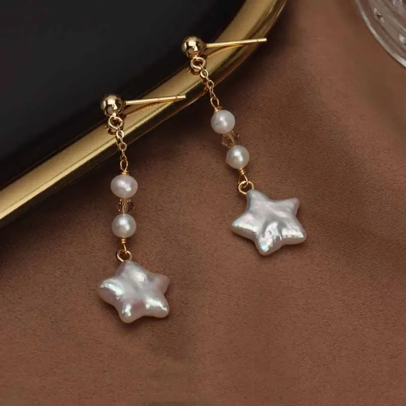 Gold-plated star-shaped freshwater pearl drop earrings by Urban Gear UG on brown fabric background