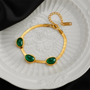 Gold bracelet with green stones on a white textured plate