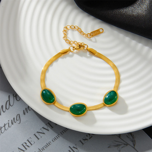Gold bracelet with green stones on a white plate