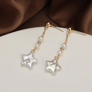 Gold-plated star-shaped freshwater pearl drop earrings by Urban Gear UG on brown fabric background