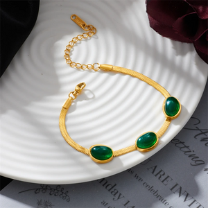 Gold bracelet with green stones on a white plate