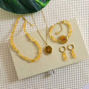 Gold jewelry set including necklaces and earrings on a textured surface with a plant in the background.