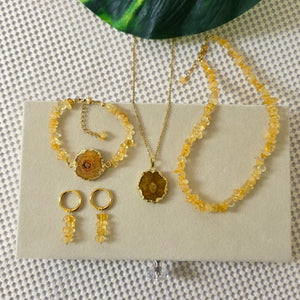 Gold jewelry set on a beige card with a green leaf in the background