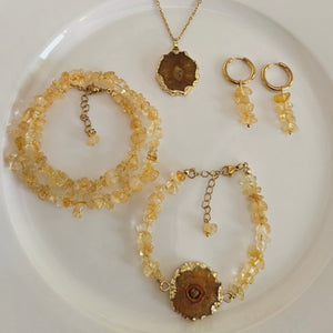 Set of gold jewelry including necklace, bracelet, and earrings on a white plate.