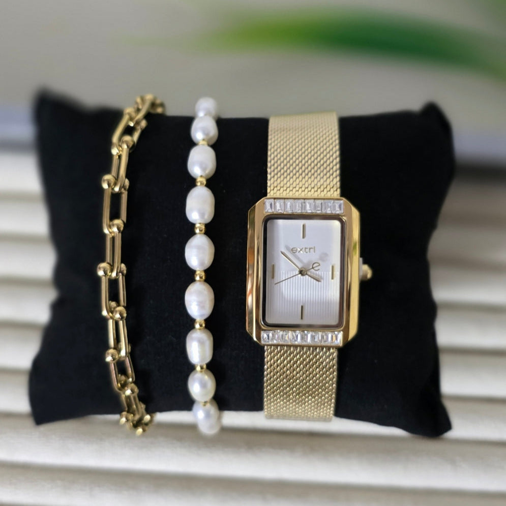 Gold watch and pearl bracelet on a black pillow with a white background