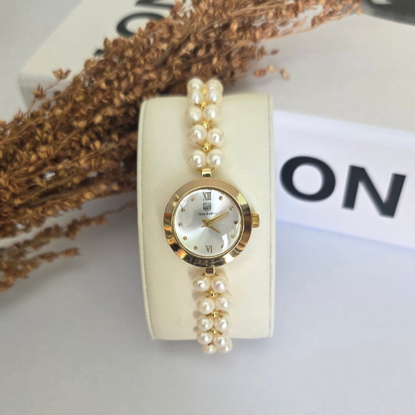 Gold watch with pearl bracelet on a white stand against a neutral background