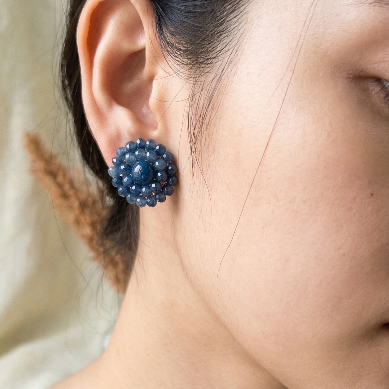 Close-up of a person wearing blue beaded earrings with a neutral background