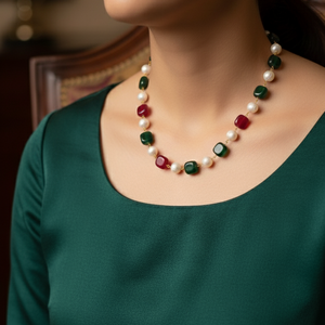 Person wearing a green top and a necklace with pearls and red and green gemstones.