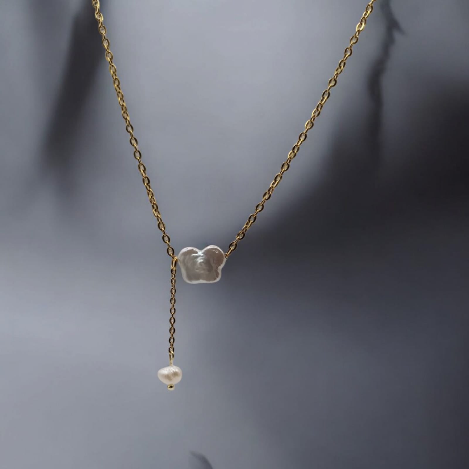 A delicate gold-plated necklace featuring a butterfly-shaped freshwater pearl pendant, styled on a soft fabric background.