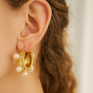 Close-up of a gold-plated baroque-style earring with freshwater pearls on model's ear