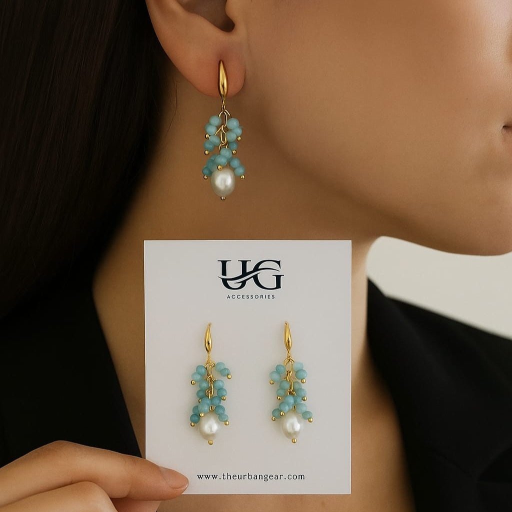 Gold earrings with turquoise stones and pearls on a branded card, held by a person.