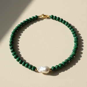 Green beaded necklace with a pearl pendant on a beige background