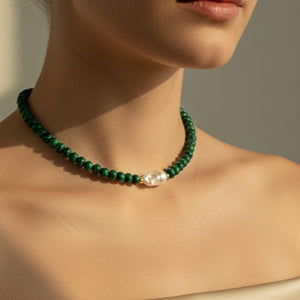 Green beaded necklace with a pearl accent on a neutral background