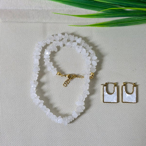 Set of jewelry including a necklace, bracelet, and earrings on a textured surface with green leaves.