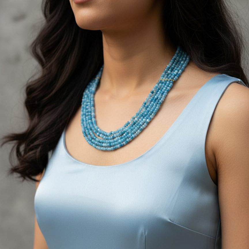 Model wearing a multi-layer blue jade mala necklace with elegant light blue outfit.