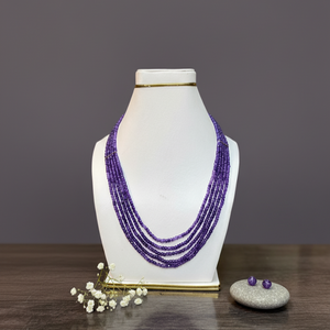Purple beaded necklace on a white mannequin bust with earrings on a wooden surface and gray background