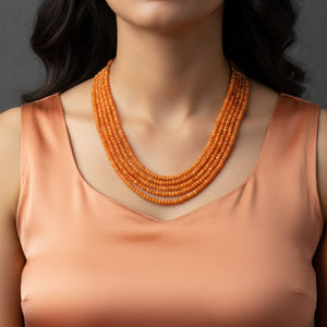 Model wearing multi-layer orange jade mala necklace on peach satin outfit.
