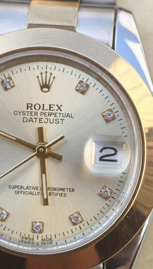 Rolex watch with gold bezel and face, featuring diamonds on a reflective surface.