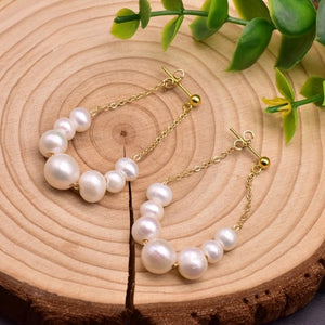 Handcrafted freshwater pearl drop earrings with gold-plated chain displayed on wooden background