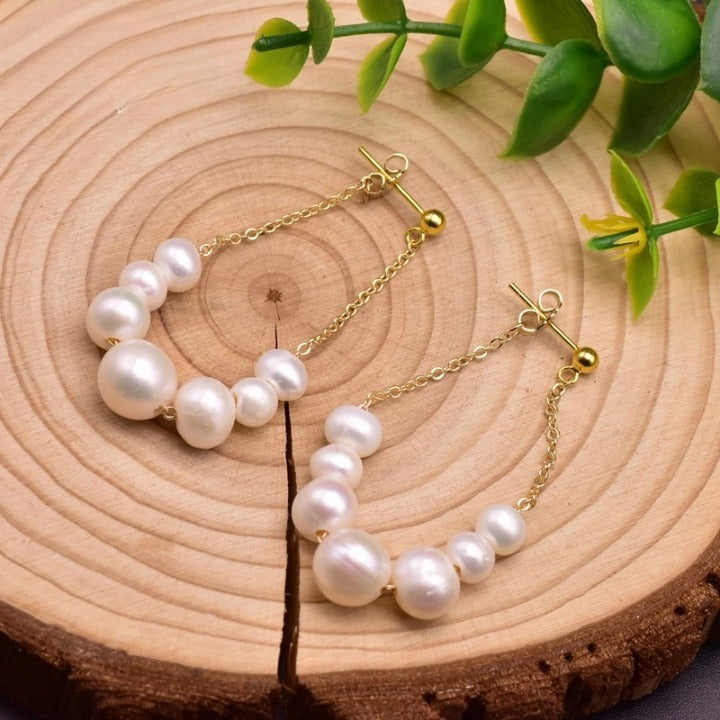 Handcrafted freshwater pearl drop earrings with gold-plated chain displayed on wooden background
