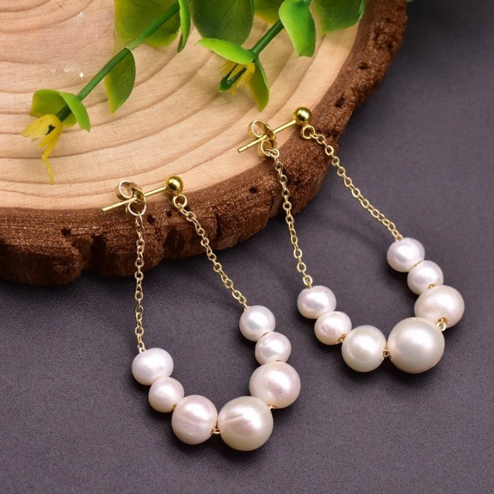 Handcrafted freshwater pearl drop earrings with gold-plated chain displayed on wooden background