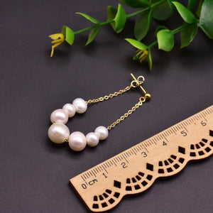 Handcrafted freshwater pearl drop earrings with gold-plated chain displayed on wooden background