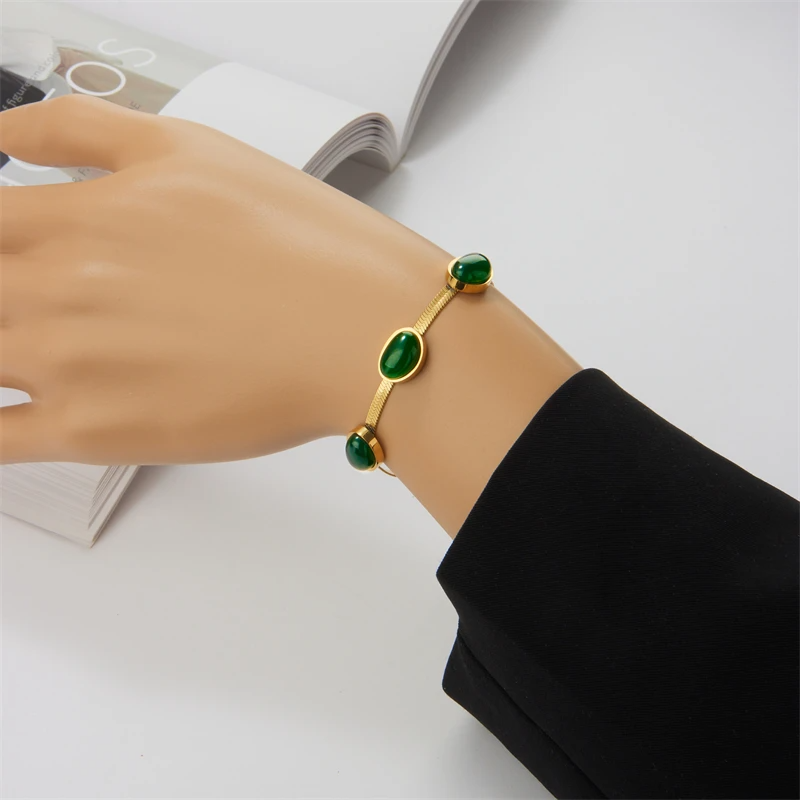 Gold bracelet with green gemstones on a mannequin hand against a white background