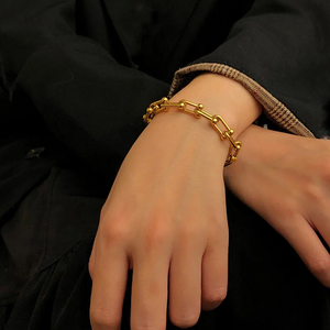 Gold chain bracelet on a wrist with a black background