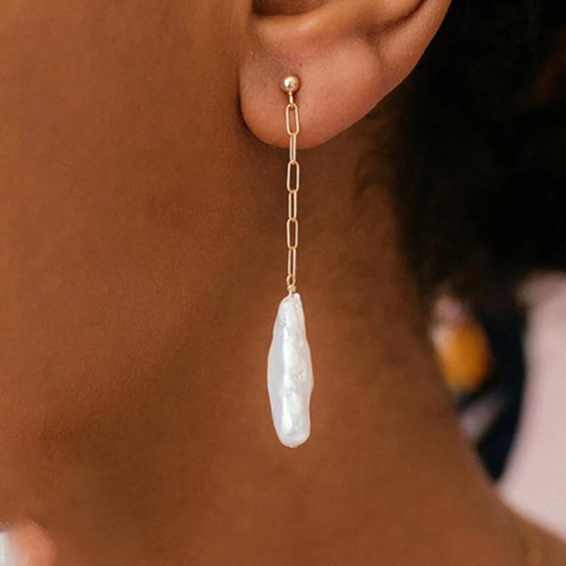 Gold earring with a pearl drop worn by a person