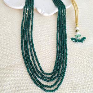 Green beaded necklace with gold accents on a textured beige surface