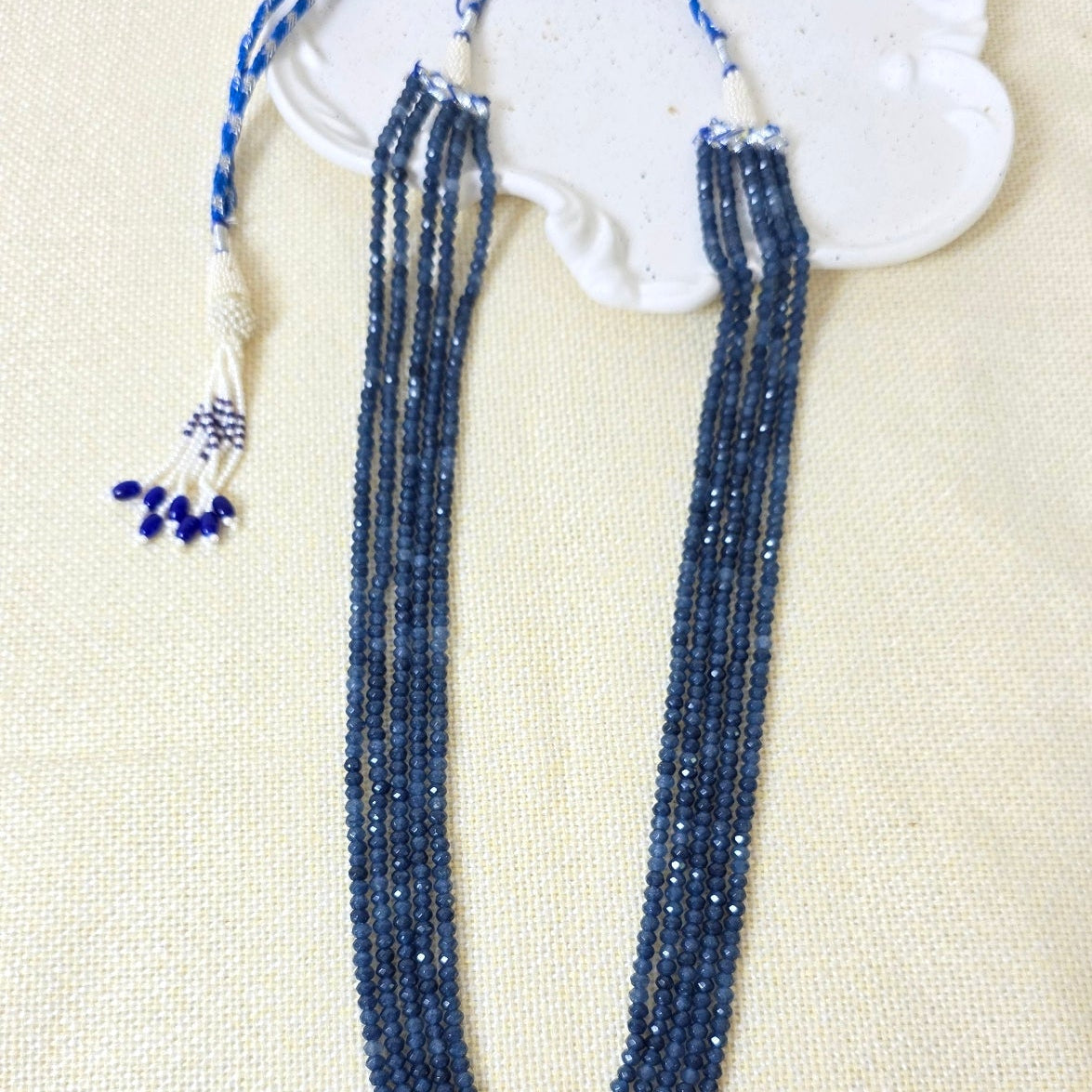 Blue beaded necklace with a white decorative element on a beige fabric background