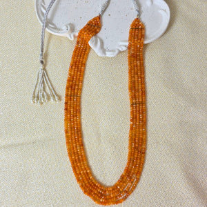 Decorative item with orange beads and white ceramic piece on a beige fabric background