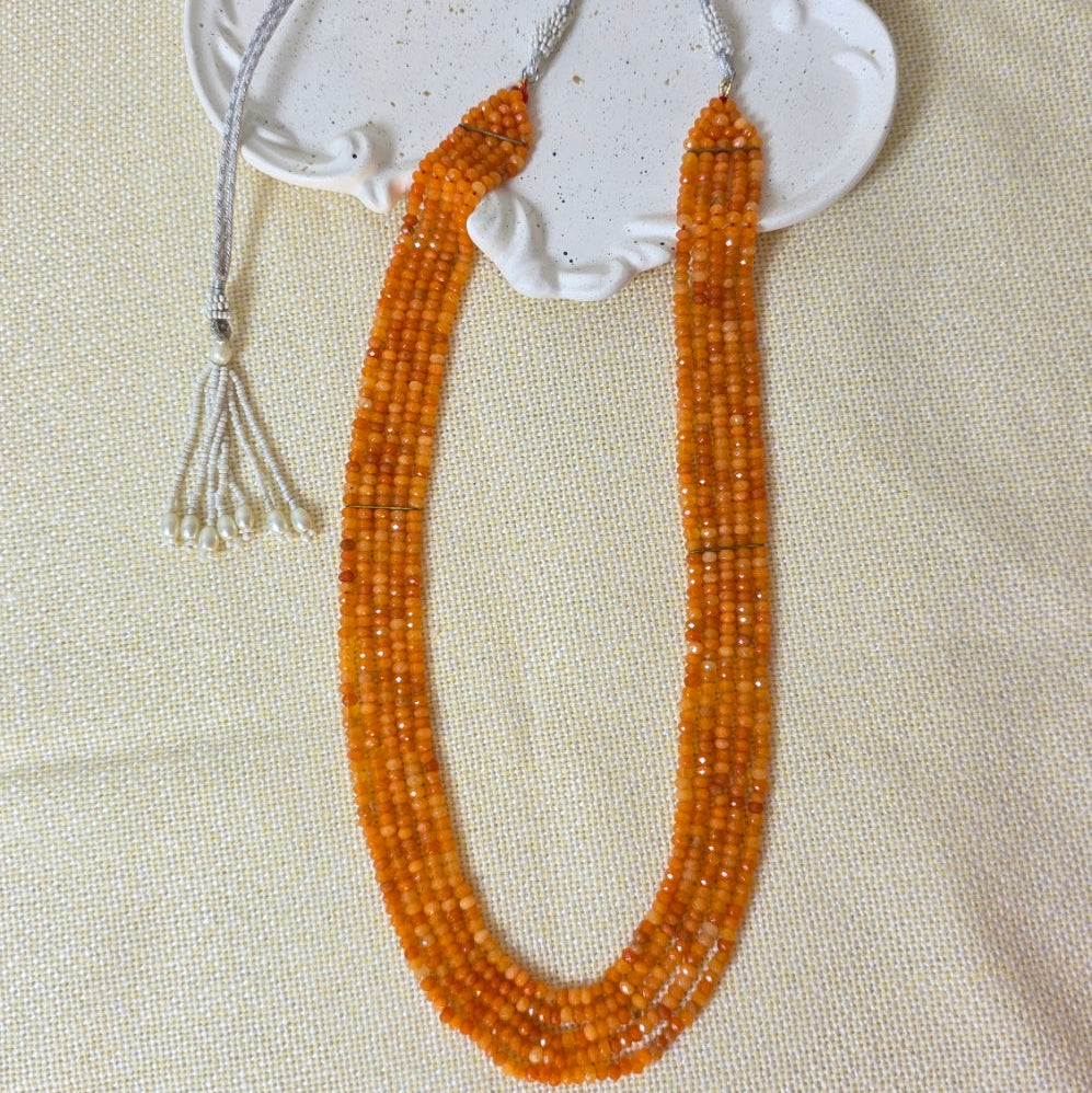 Decorative item with orange beads and white ceramic piece on a beige fabric background