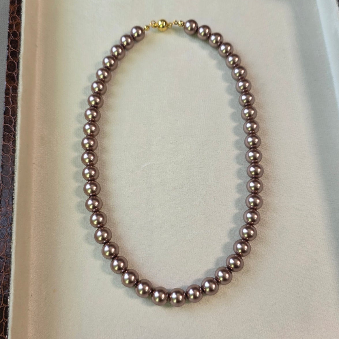 Magnetic metallic brown pearl necklace with gold magnetic clasp displayed in a jewelry box.