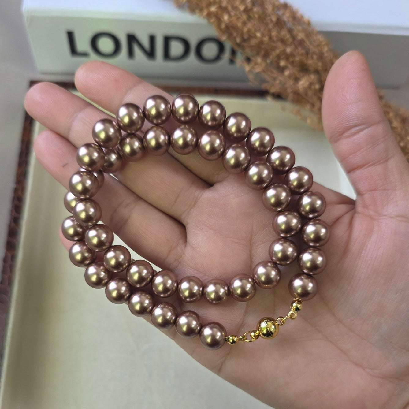 Magnetic metallic brown pearl necklace with gold magnetic clasp displayed in a jewelry box.