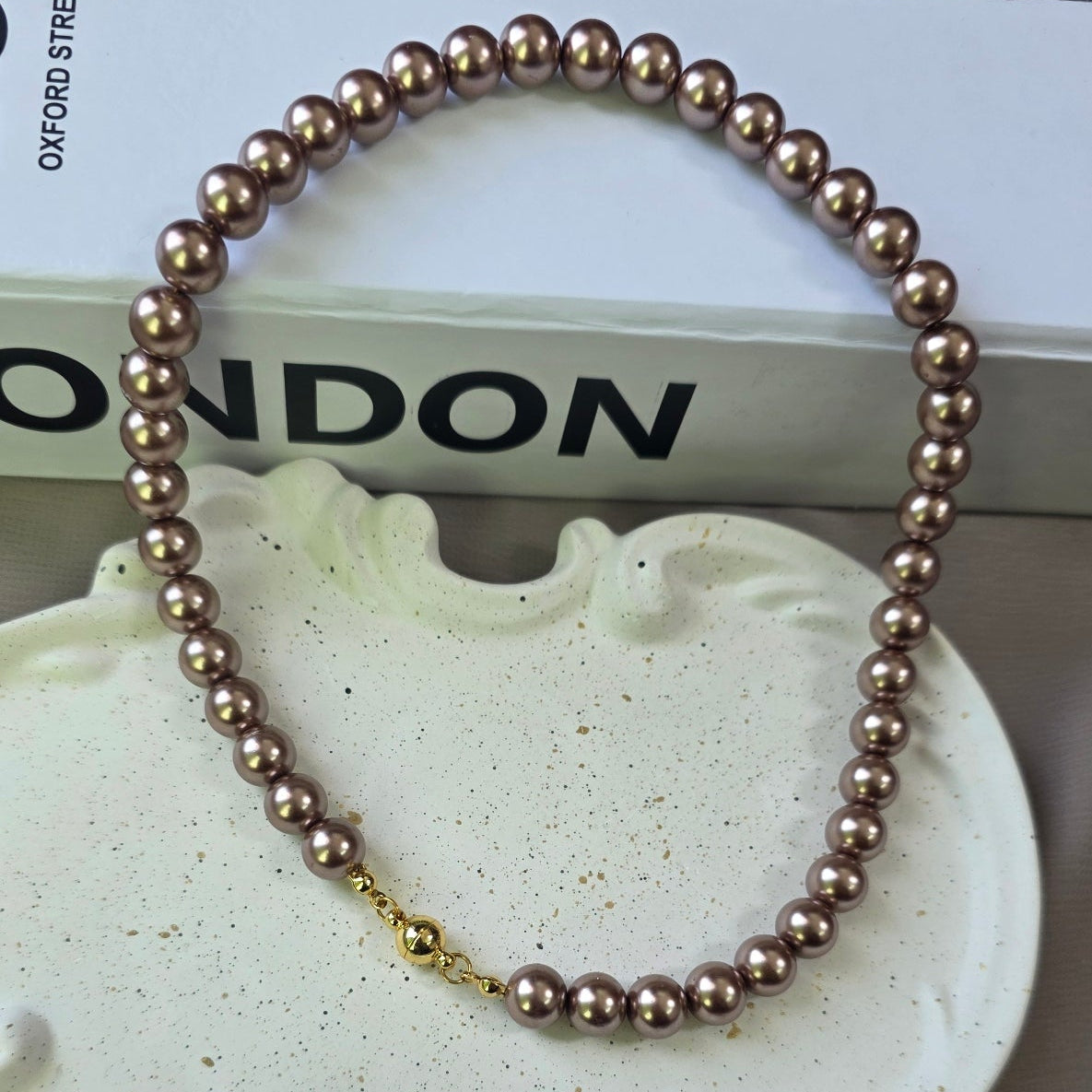Magnetic metallic brown pearl necklace with gold magnetic clasp displayed in a jewelry box.