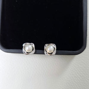 Pearl stud earrings on a black earring stand against a white background
