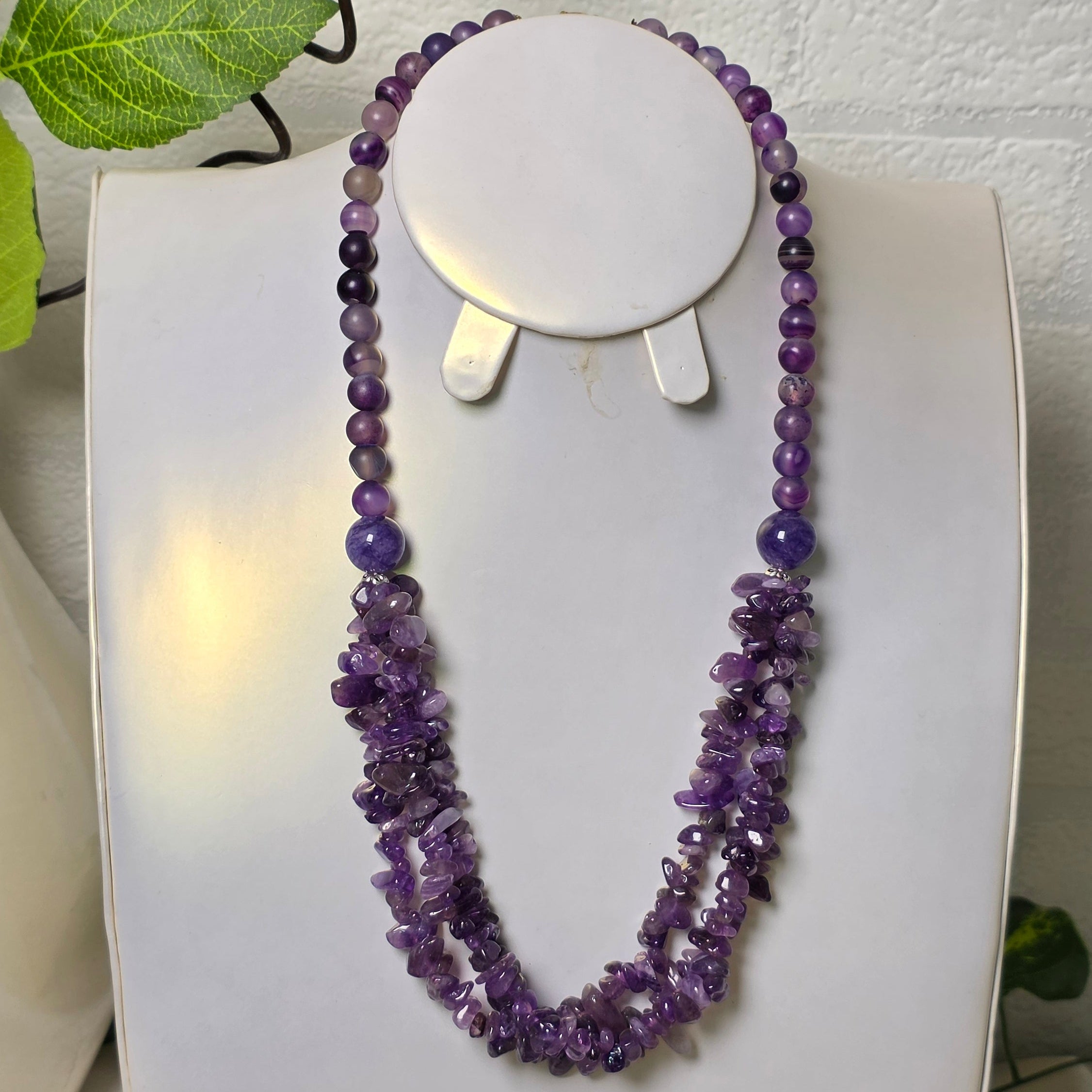 Purple beaded necklace on a white stand with a soft focus background