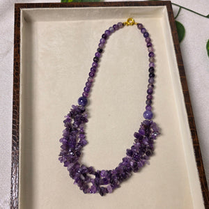 Purple beaded necklace on a white tray with green leaves in the background