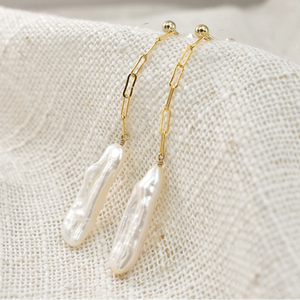 Pearl earrings with gold chains on a textured beige surface, branded 'OriginaIngenu'.