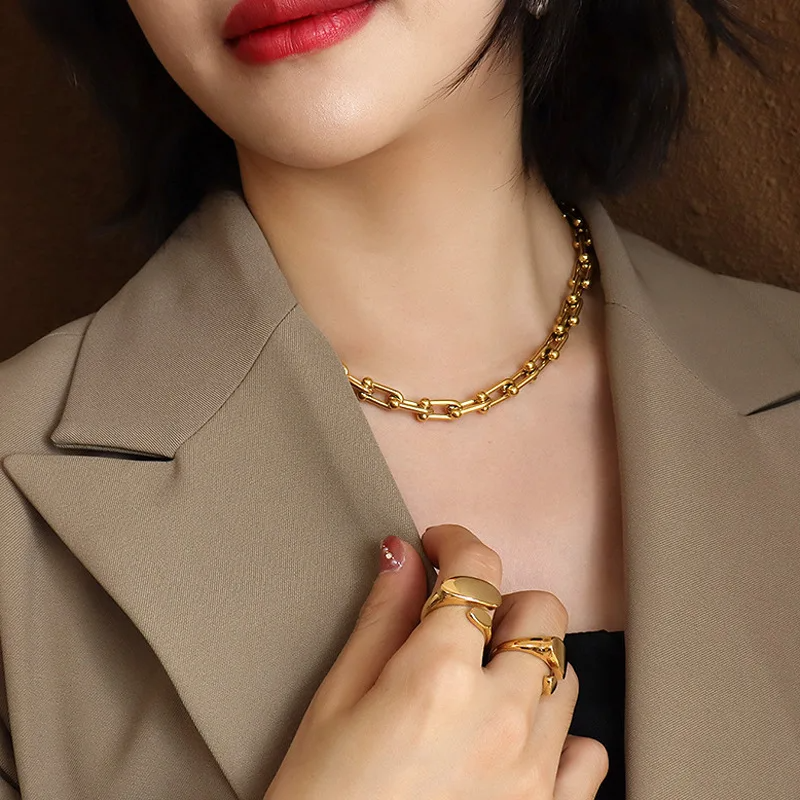 Woman wearing a gold chain necklace and rings, with a blurred background