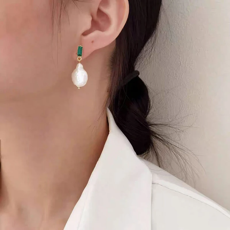 Pearl earring with green gemstone on a blurred background