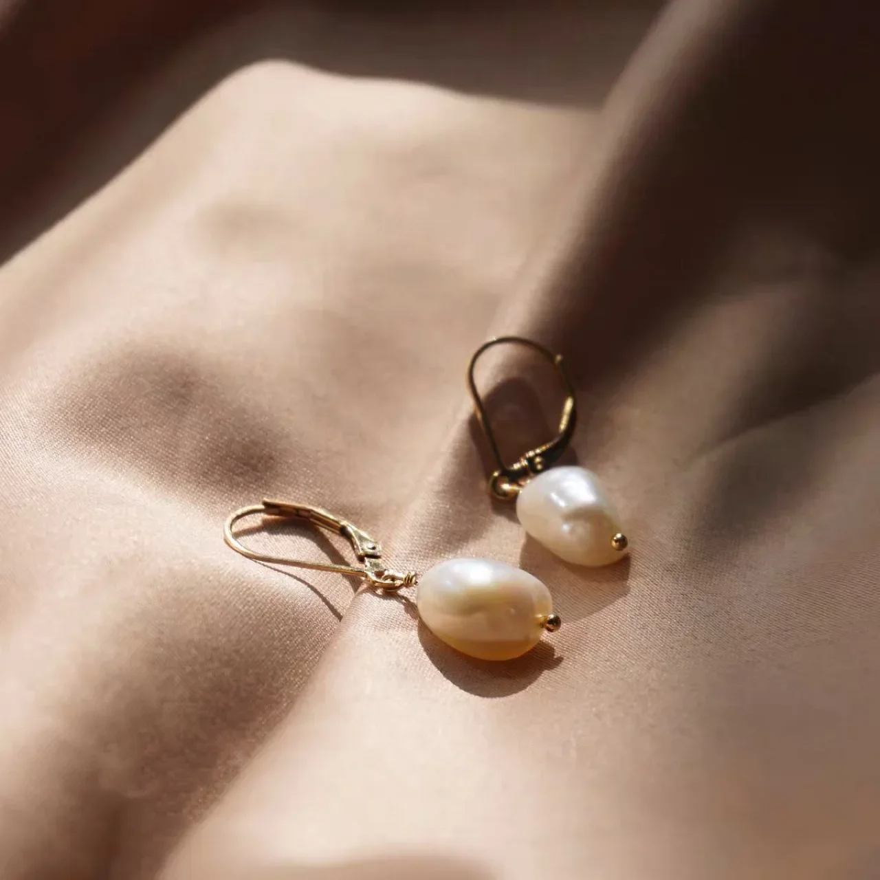 Elegant freshwater pearl drop earrings with gold lever-back hooks on white fabric background.