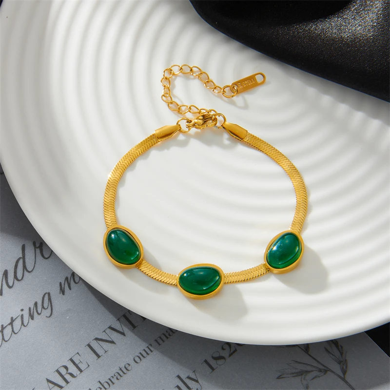 Gold bracelet with green stones on a white plate