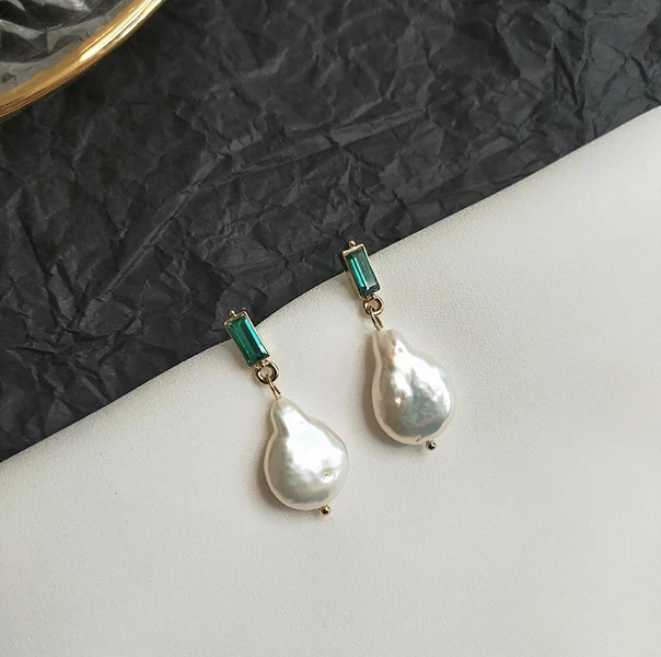 Pearl earrings with green gemstones on a white surface and black textured background