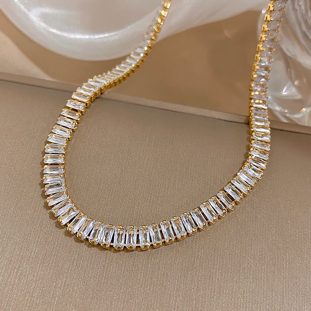 Gold and diamond necklace on a beige surface with a decorative dish in the background