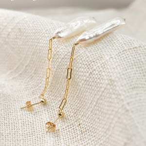 Pearl and gold chain earrings on a textured beige surface