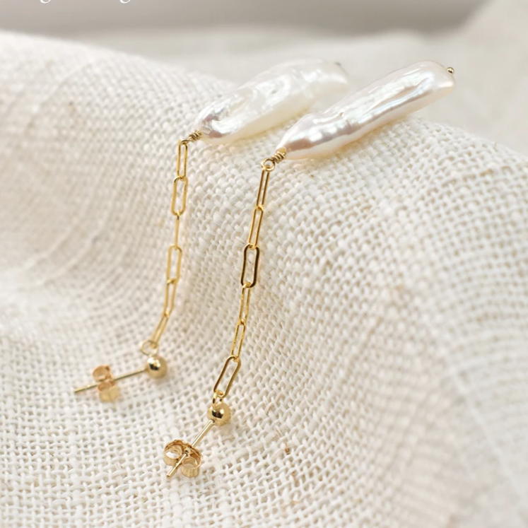 Pearl and gold chain earrings on a textured beige surface